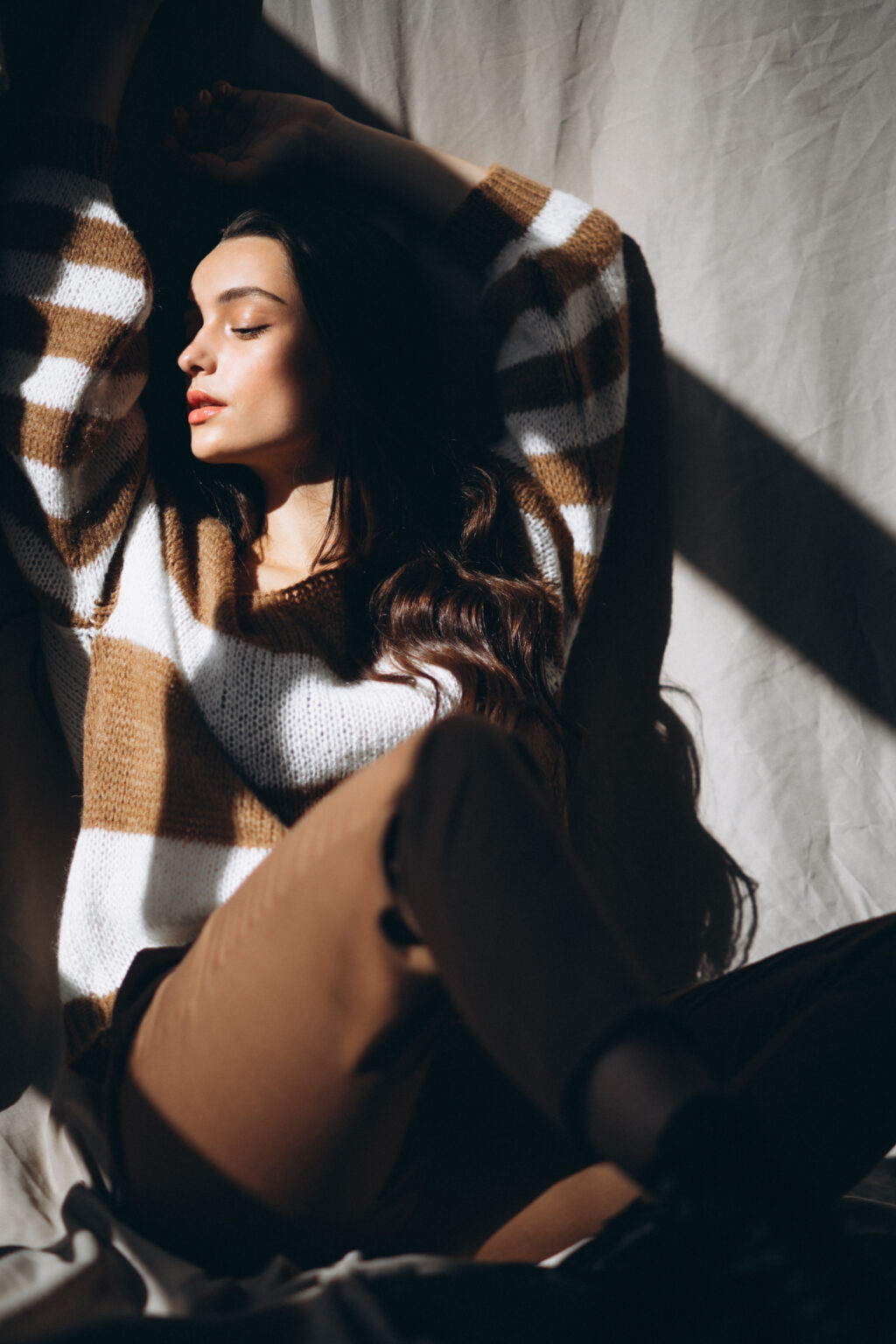 Young woman in a warm sweater sitting on ground in studio